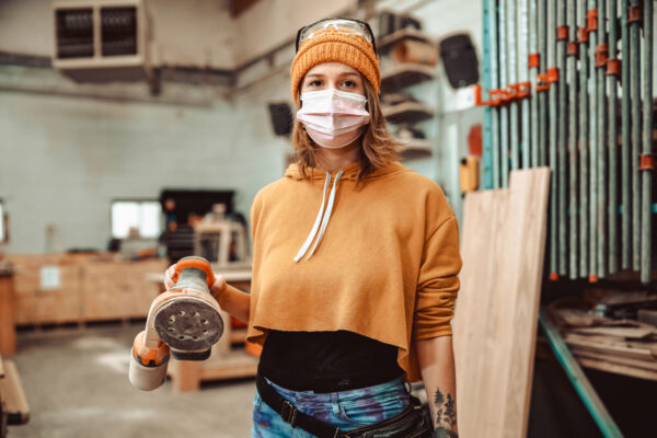 Young Female Artist Using Power Tools At The Wood Shop